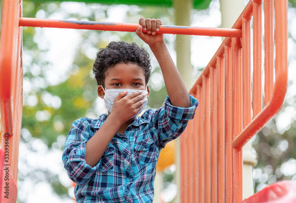 Obraz premium Coronavirus or COVID-19 and Air pollution pm 2.5 concept. Little boy playing at playground and wearing protective medical mask on face for protect PM 2.5 or spreading of disease virus.