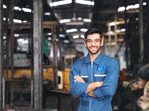 Cuadro en lienzo Smiling worker in safety glassess standing with arm crossed near industrial equi