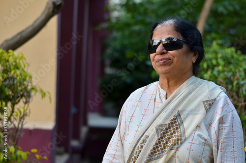 Portrait of a happy retired Indian woman wearing UV-protecting sunglasses for physical protection of eye immediately after surgery. Showing a victory sign - defeat cataract  photo