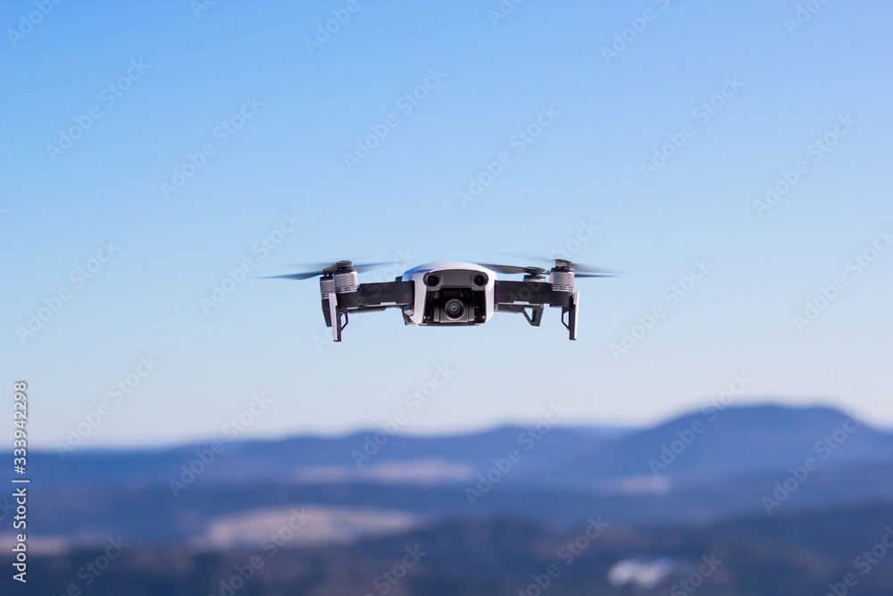 Quadcopter drone in flight at blue sky and mountains background Quadcopter drone in flight at blue sky and mountains background