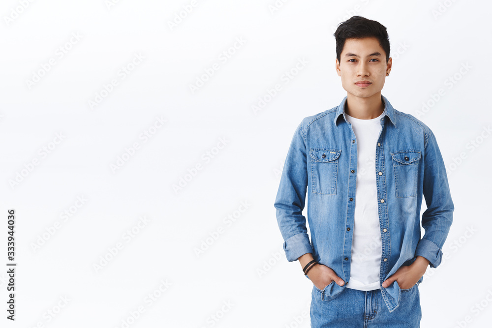 Portrait of determined, confident handsome asian guy in denim clothes, holding hands in pockets, casual pose, smiling at camera, ready to receive orders from boss, white background Portrait of determined, confident handsome asian guy in denim clothes, holding hands in pockets, casual pose, smiling at camera, ready to receive orders from boss, white background