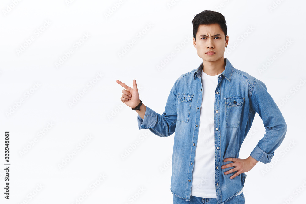 Portrait of serious-looking angry young asian guy scolding person for making big mistake, pointing finger left at something disturbing and bad, frowning and squinting judgemental, white background Portrait of serious-looking angry young asian guy scolding person for making big mistake, pointing finger left at something disturbing and bad, frowning and squinting judgemental, white background