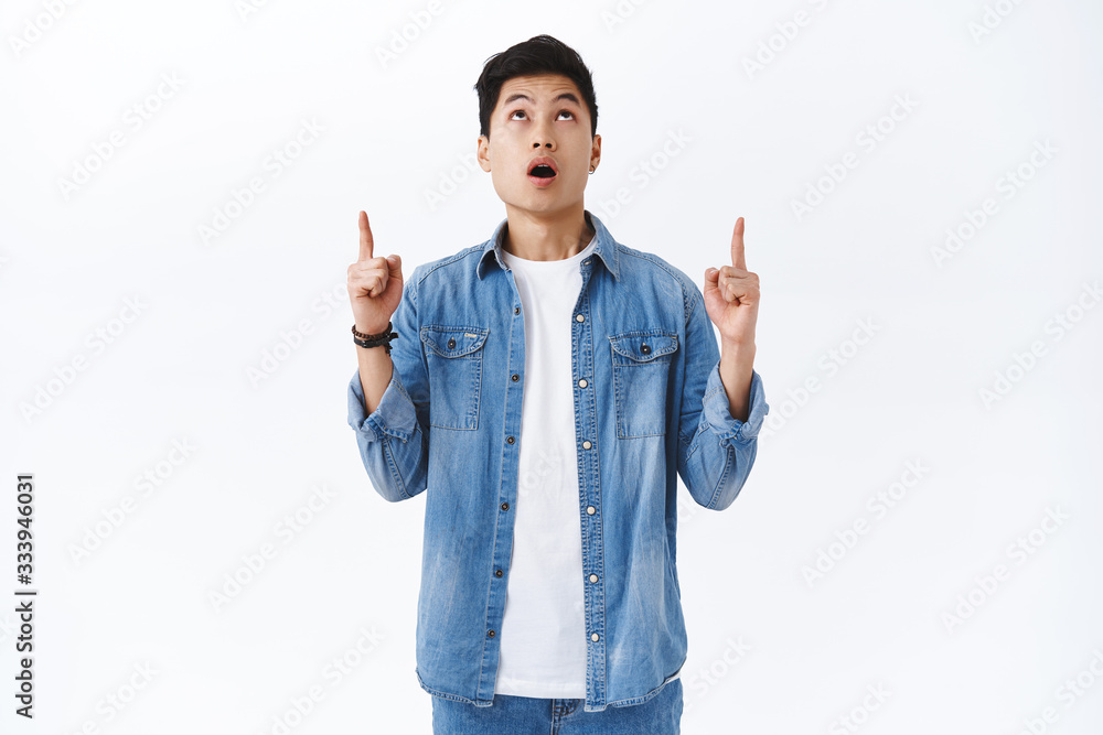 Portrait of impressed young surprised asian man gasping, open mouth astonished and looking pointing fingers up at something incredible, unbelievable super cool offer, white background Portrait of impressed young surprised asian man gasping, open mouth astonished and looking pointing fingers up at something incredible, unbelievable super cool offer, white background