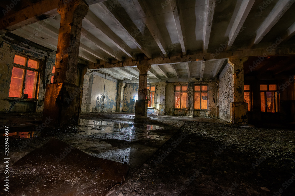 Interior of an old abandoned soviet building with cracked ragged walls and leaking roof and wet floor at night with flashlights of stalkers