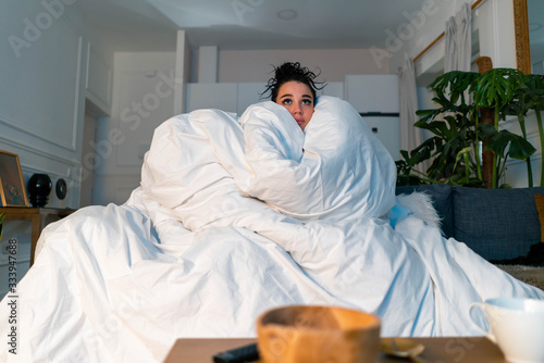 Woman Under Blanket Watching News About SARS Coronavirus, 2019-nCoV. Fear Of Pandemia. Stay Home Concept. Not Leave Home. Quarantine.