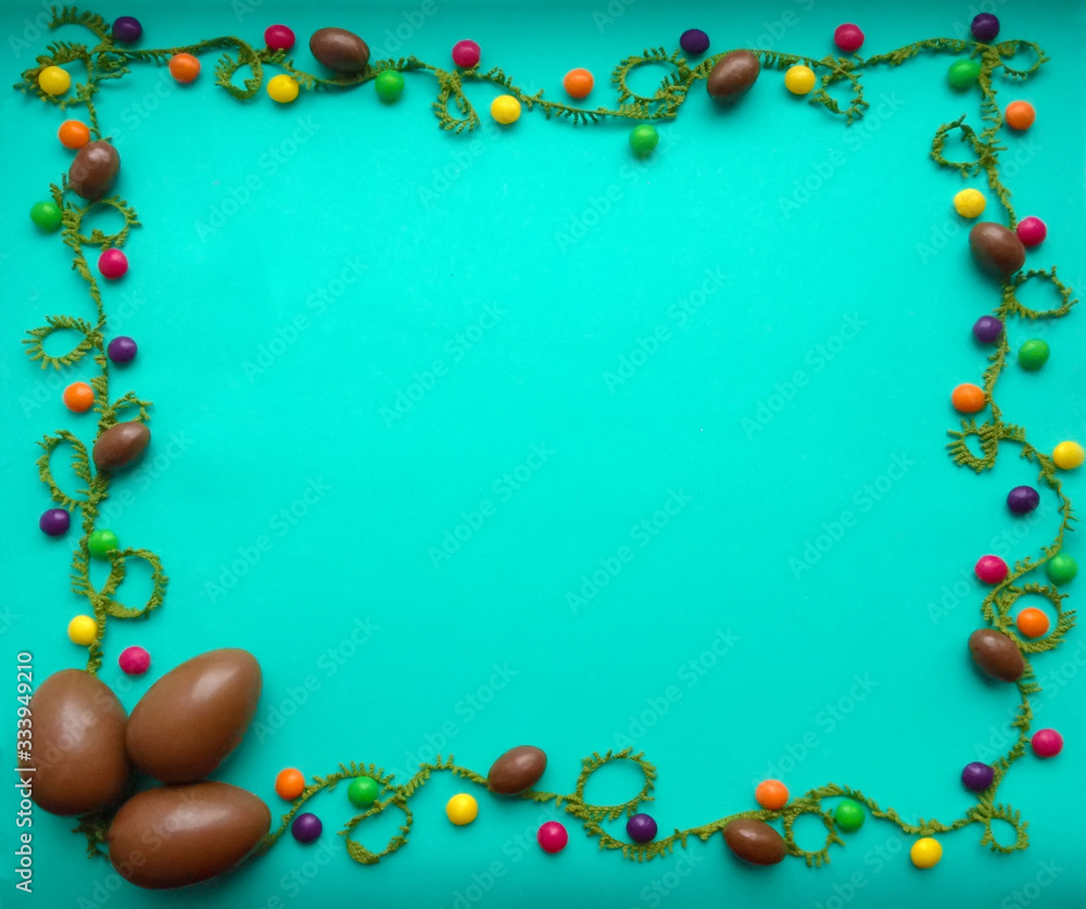 Chocolate eggs and multi-colored candy on a green background