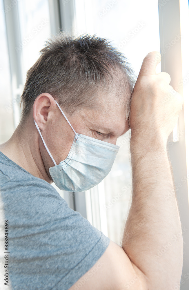 Sick man in medical protective face mask looking through window. Coronavirus pandemic covid-19 and quarantine concept.