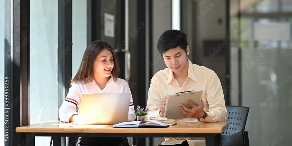 Photo of young business developer team discussing/meeting/working with computer laptop and tablet while sitting together at wooden working desk over orderly living room as background. Photo of young business developer team discussing/meeting/working with computer laptop and tablet while sitting together at wooden working desk over orderly living room as background.