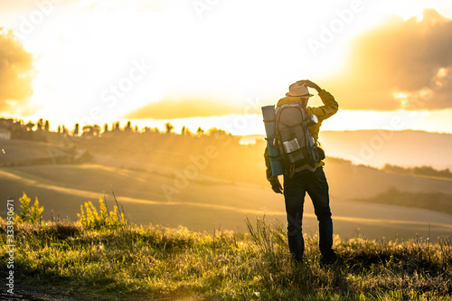 Young man trekker in tuscany hills at sunset. Yellow jacket, backpack, hat. Traveling Volterra, Italy. photo