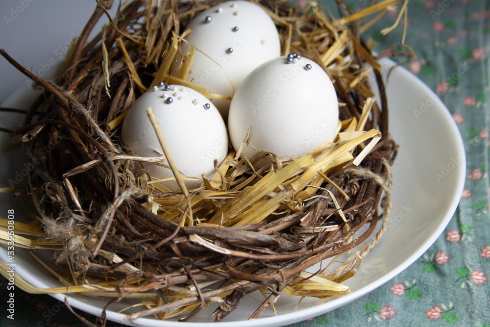 white eggs lie on a white plate with a nest and hay decor