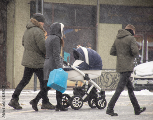 Family walking with the child in the stroller in snowy winter day. Intentional motion blur.