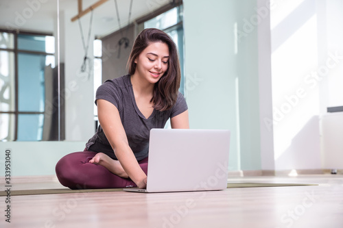 Photo of young woman practicing yoga with laptop during pandemia. Beautiful girl practice yoga in class. Yoga studio instructor. Blurred background.
