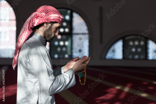 Young Arabic Muslim man  praying. Doing a dailly pray inside modern beautiful mosque. photo