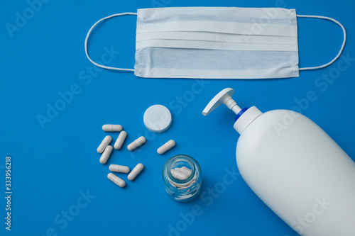 facial disposable medical mask, white pills and liquid hand soap isolated on blue background.