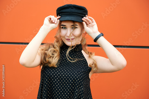 Photo of a fashionable blonde girl in a dress on an orange wall background outdoors in spring city