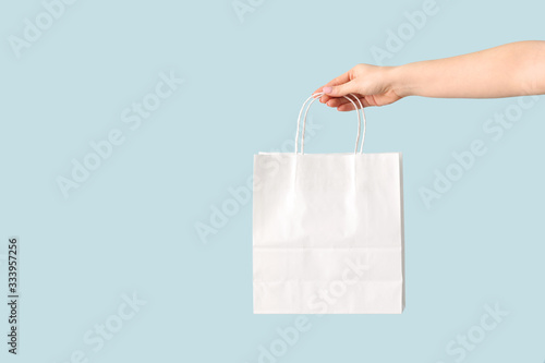 Female hand with paper shopping bag on color background photo