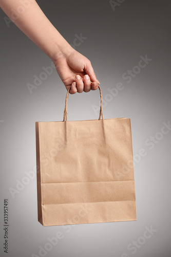 Female hand with paper shopping bag on grey background