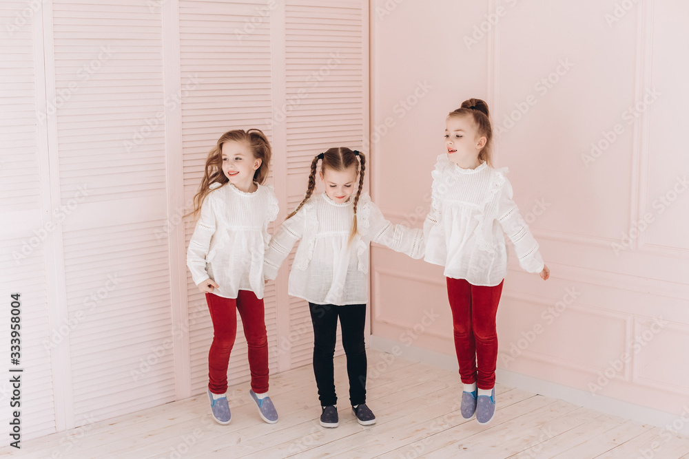 Fototapeta premium Happy cute adorable caucasian triplets girls posing at home together. Childhood, children, twins concept. Smiling girls playing together