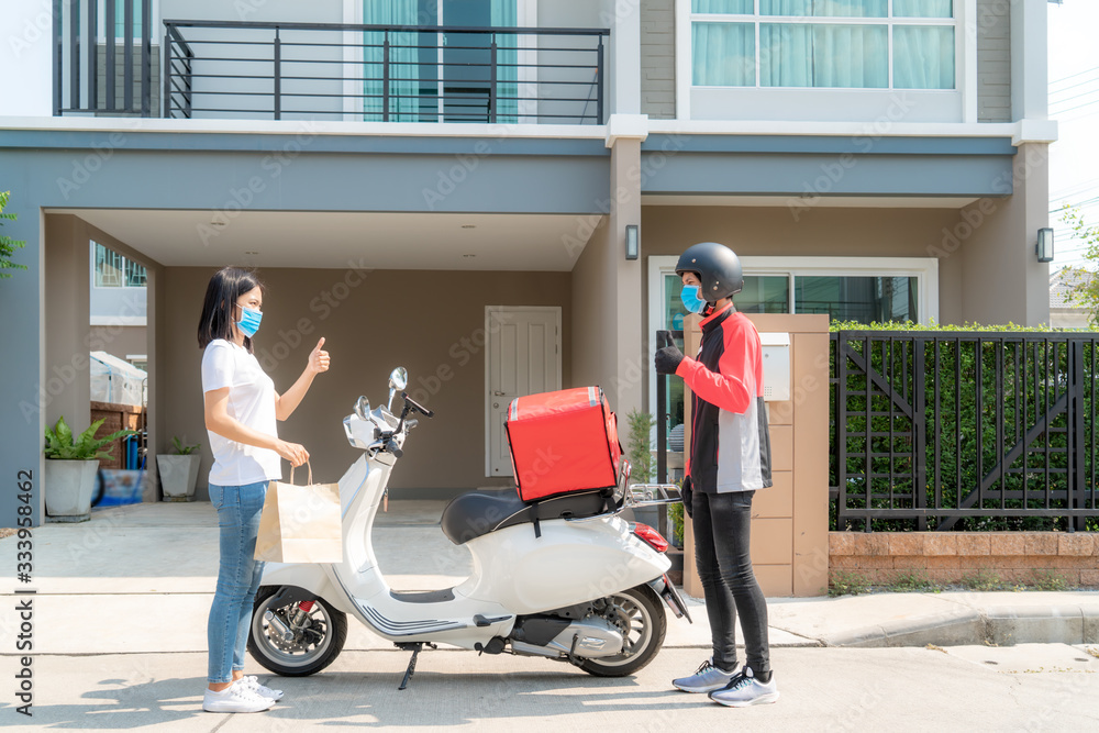 Asian woman pick up delivery food bag from box and thumb up form contactless or contact free from delivery rider with bicycle in front house for social distancing for infection risk.