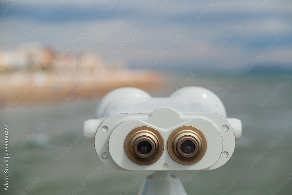 Binoculars telescope for travelers. Observation deck overlooking the Mediterranean sea and the beach. Large white binoculars on a stand against the cloudy sky. Selective focus