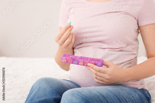 Young pregnant woman with pills box at home