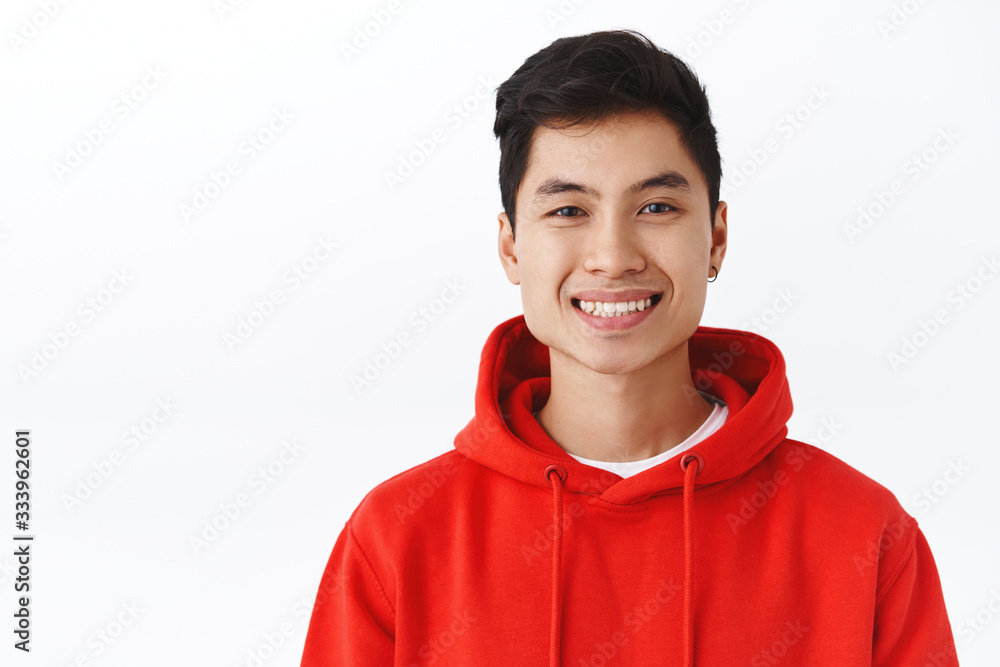 Close-up portrait of enthusiastic, attractive asian male student in red hoodie, earring, smiling cheerful camera, looking happy, pleased and satisfied, standing white background Close-up portrait of enthusiastic, attractive asian male student in red hoodie, earring, smiling cheerful camera, looking happy, pleased and satisfied, standing white background