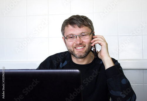 A businessman in front of a laptop is smiling and talking on a mobile phone.