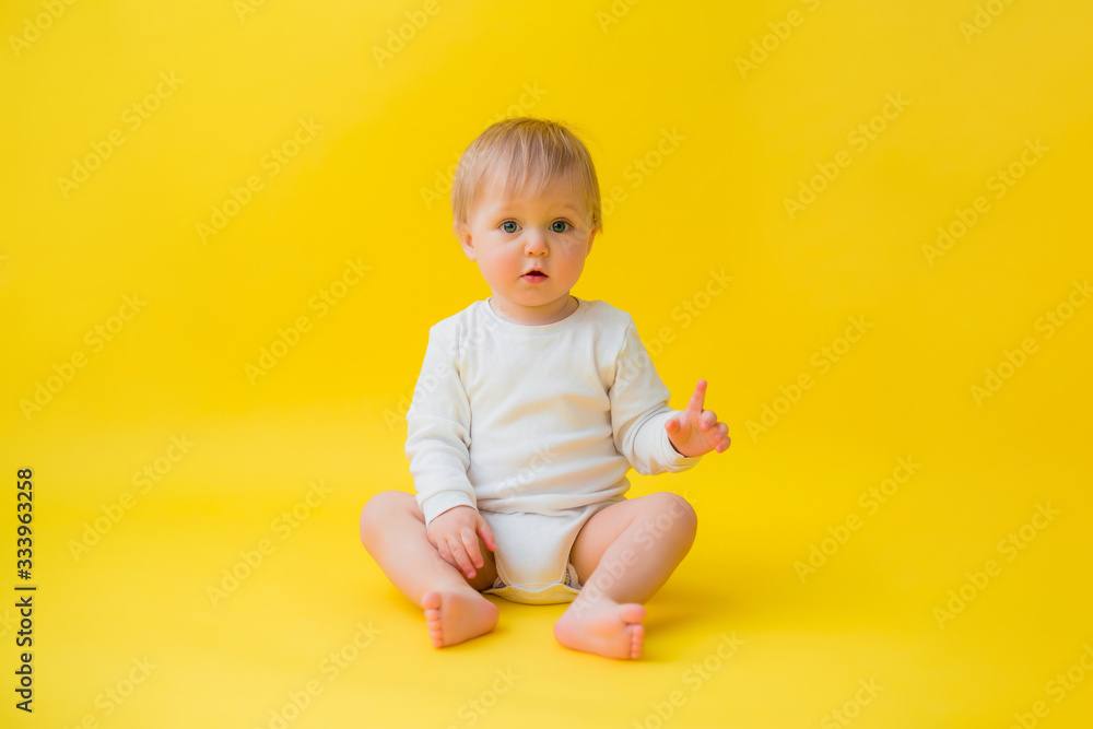 Healthy baby in white bodysuit sits on a yellow background, space for text Healthy baby in white bodysuit sits on a yellow background, space for text