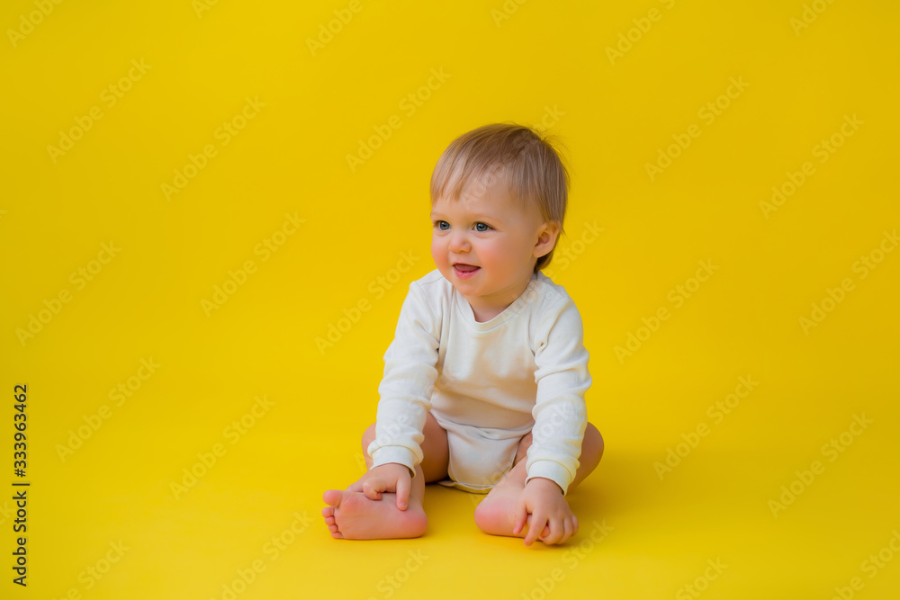 Healthy baby in white bodysuit sits on a yellow background, space for text Healthy baby in white bodysuit sits on a yellow background, space for text
