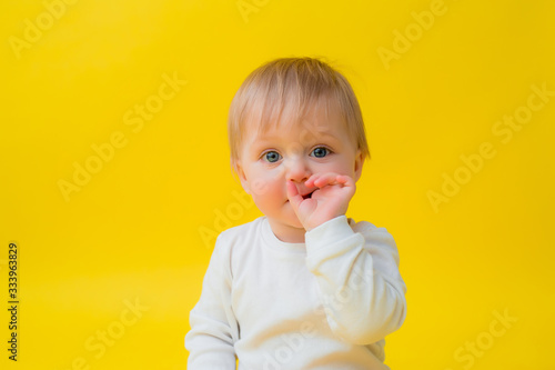 Healthy baby in white bodysuit sits on a yellow background, space for text