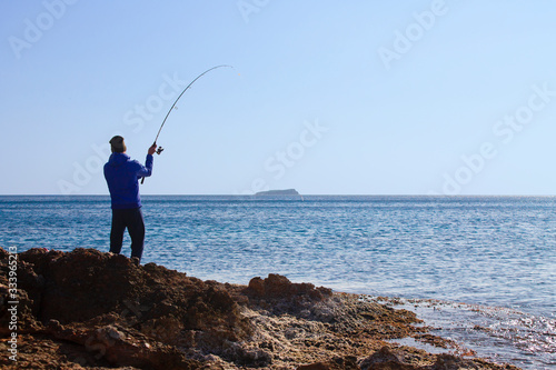Photo An unrecognizable male fisherman stands on the beach and throws a fishing rod