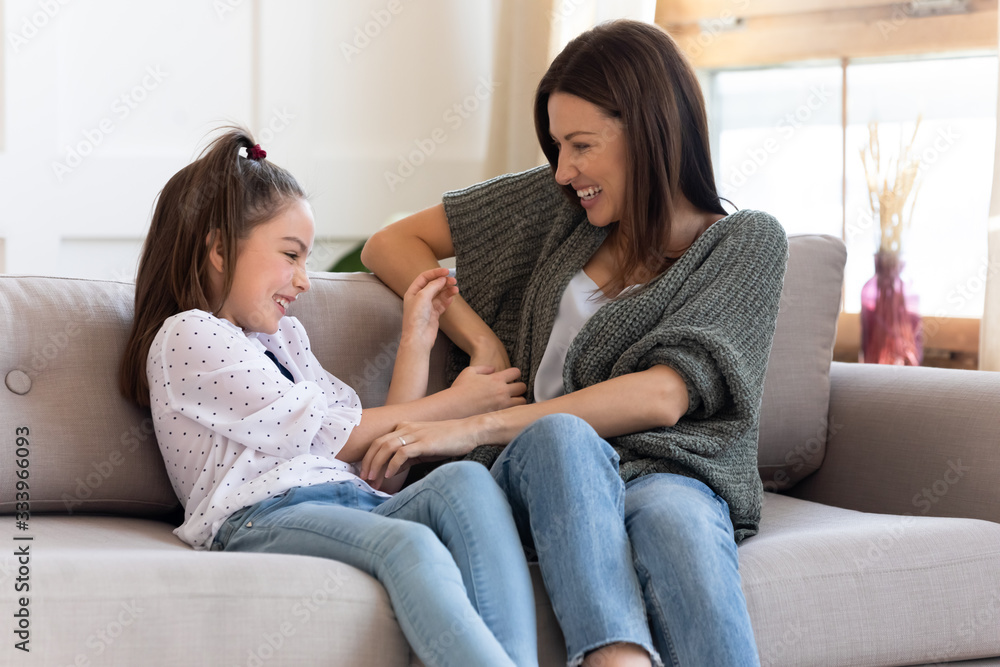 Laughing overjoyed school age girl having fun with beautiful mommy, relaxing together on cozy couch at home. Attractive young mother tickling adorable child daughter, entertaining in living room. Laughing overjoyed school age girl having fun with beautiful mommy, relaxing together on cozy couch at home. Attractive young mother tickling adorable child daughter, entertaining in living room.