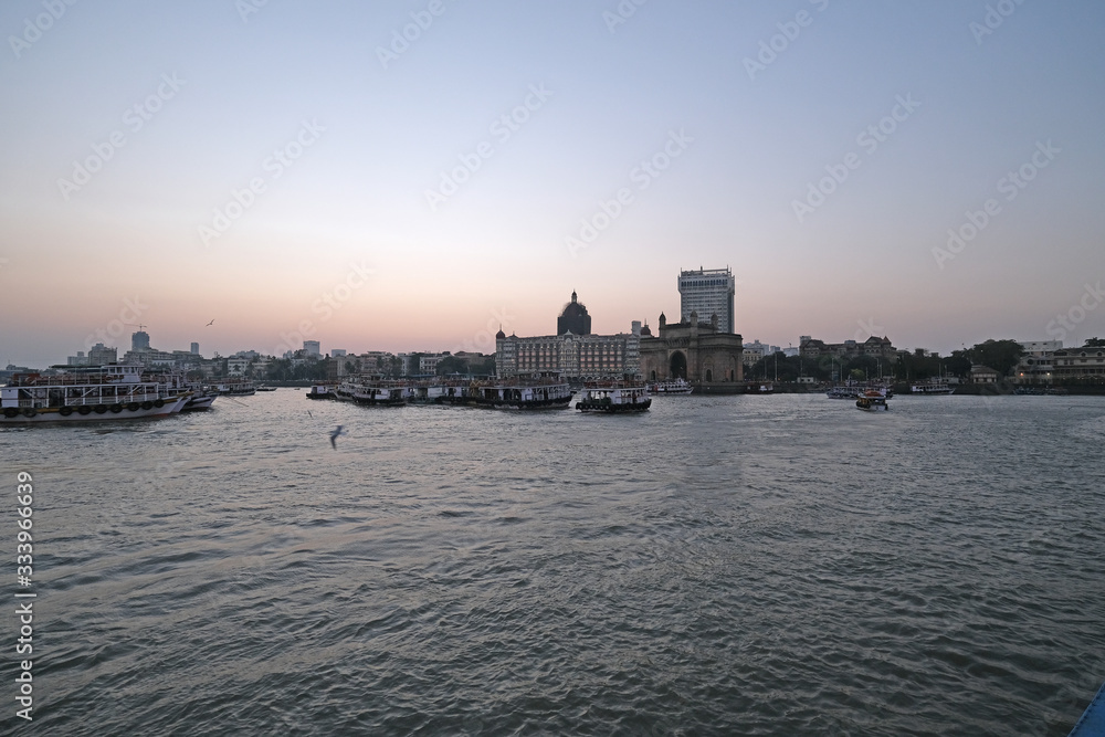 Fototapeta premium Taj Mahal hotel, Gateway of India and tourist boats in water of Arabian Sea on sunset in Mumbai, India