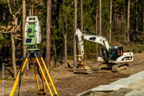 Surveyors equipment (theodolite or total positioning station) on the construction site of the road or building with construction machinery background