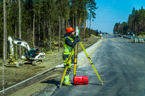 Surveyor engineer with equipment (theodolite or total positioning station) on the construction site of the road or building with construction machinery background