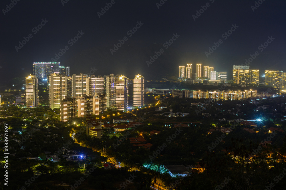 Obraz premium Night view of Sanya city with bright multi-colored illumination buildings, structures, roads, sidewalks, poles, bridges.