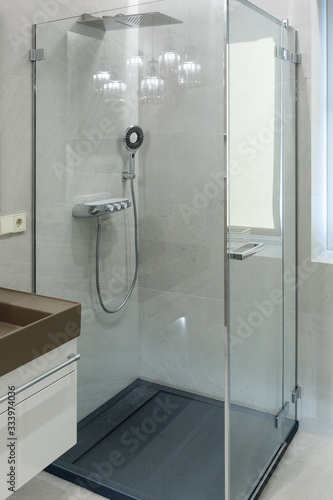 Shower cabin with transparent glass walls, rain shower and shower head. Modern bathroom design.