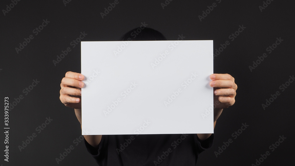 female model's hands is holding the A4 paper on black background. female model's hands is holding the A4 paper on black background.