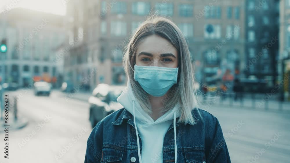 Young serously woman in medical mask standing in city street looking to camera road with cars on background Concept of health and safety life COVID-19 coronavirus virus protection pandemic in world Young serously woman in medical mask standing in city street looking to camera road with cars on background Concept of health and safety life COVID-19 coronavirus virus protection pandemic in world