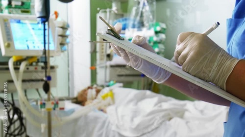 Doctor Writing Medical Prescription and Patient on Lung Ventilation in Intensive Care Unit
