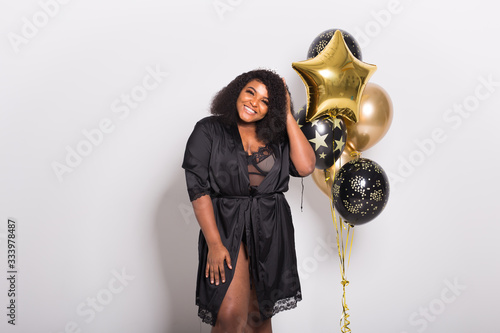 Holidays, party and fun concept - Portrait of smiling young African-American young woman looking stylish on white background holding balloons.