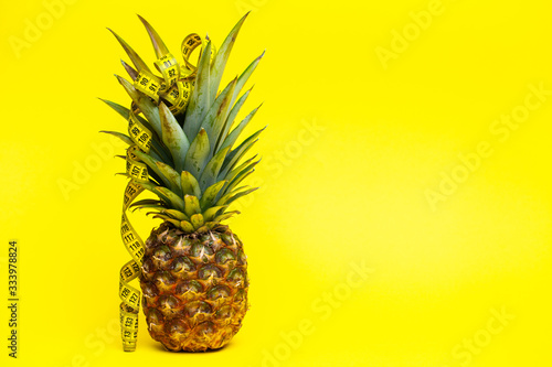 Ripe pineapple with tape measure on a yellow background.
