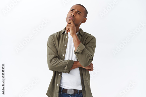 Hmmm interesting. Portrait of thoughtful handsome, smart african american man thinking, making choice, squinting and looking up, pondering decision, standing white background photo