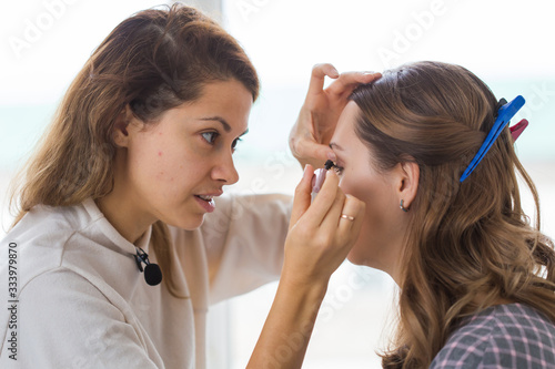 Beauty and cosmetics concept - Makeup artist doing professional make up of young woman