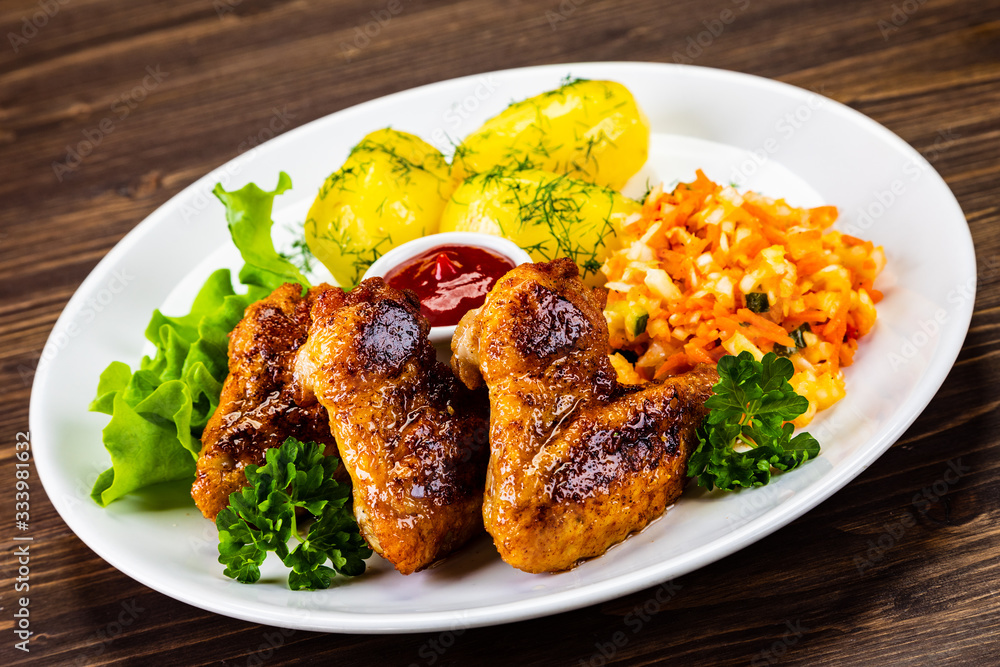 Fried chicken wings with boiled potatoes and vegetable salad on wooden board Fried chicken wings with boiled potatoes and vegetable salad on wooden board