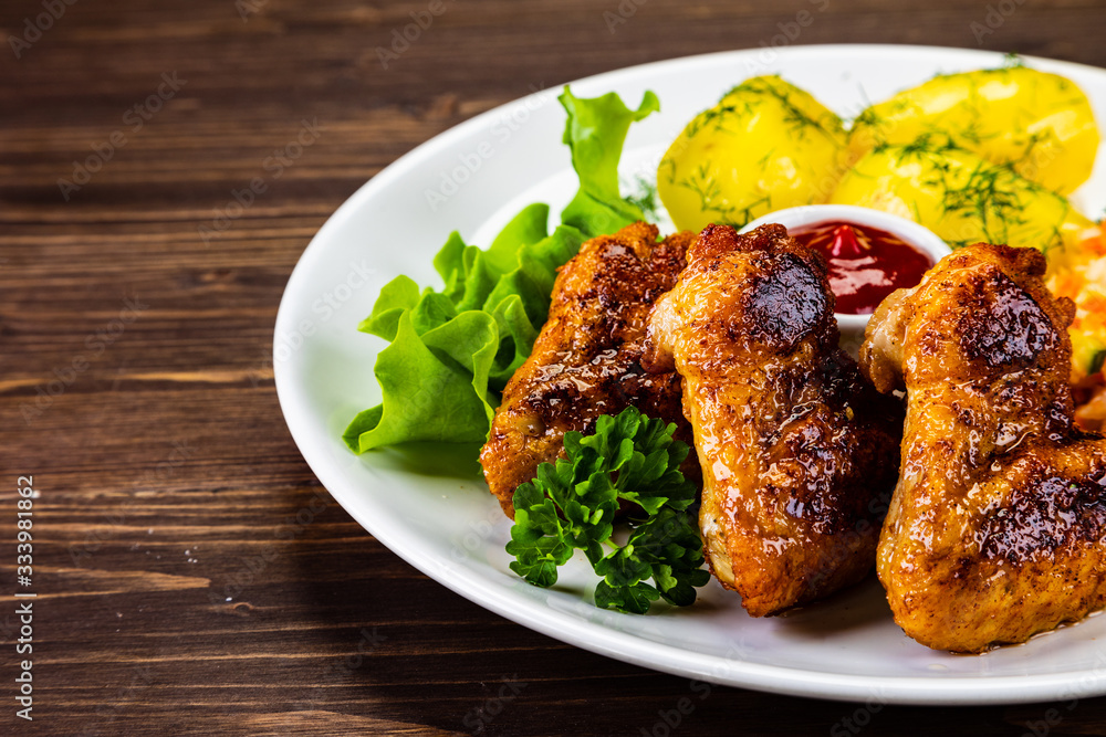 Fried chicken wings with boiled potatoes and vegetable salad on wooden board Fried chicken wings with boiled potatoes and vegetable salad on wooden board