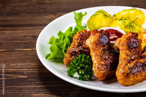 Fried chicken wings with boiled potatoes and vegetable salad on wooden board