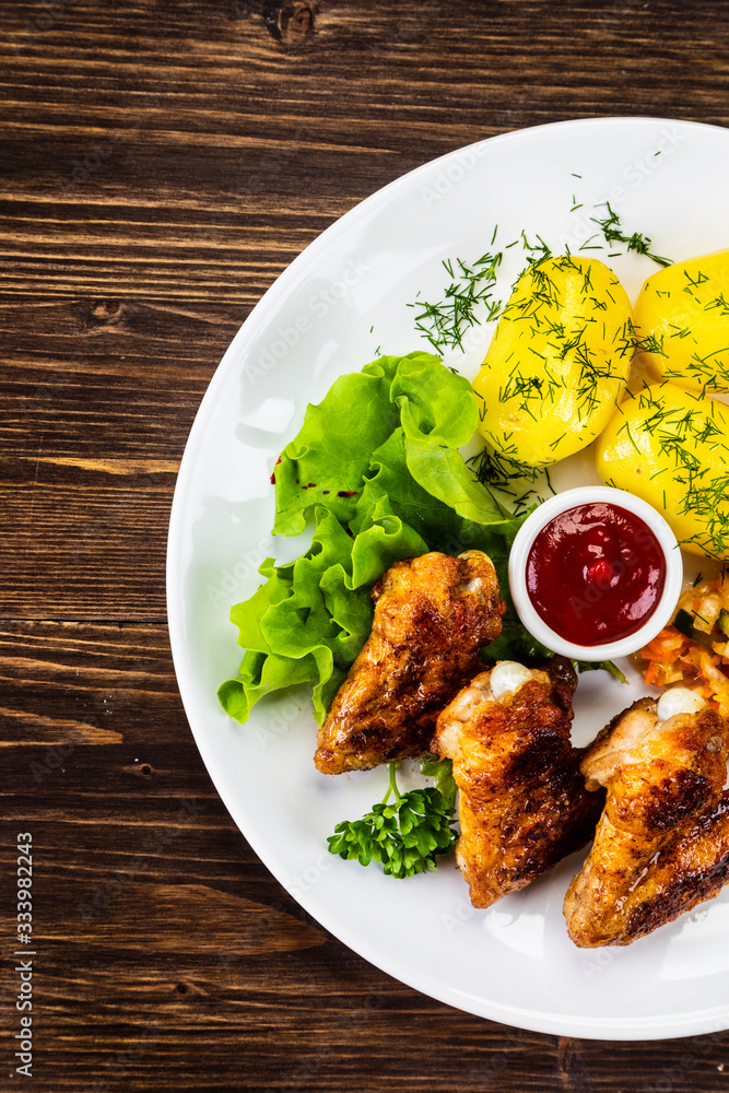 Fried chicken wings with boiled potatoes and vegetable salad on wooden board Fried chicken wings with boiled potatoes and vegetable salad on wooden board