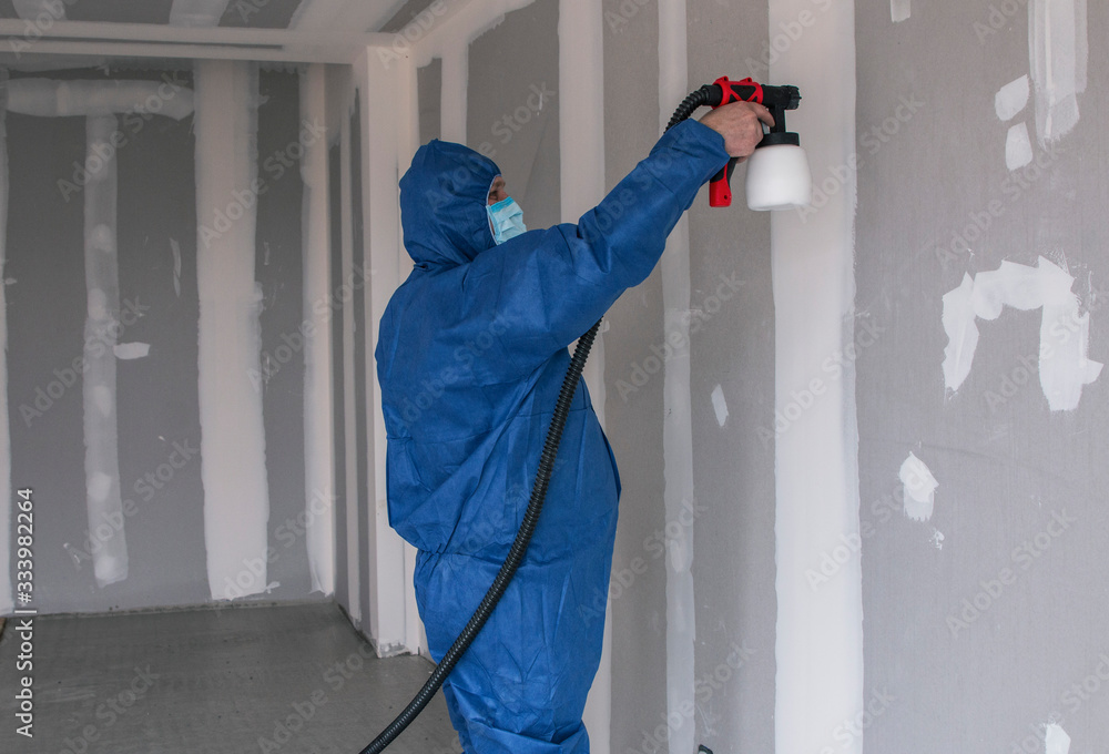 a man in a special suit paints walls with a spray gun, painting walls and ceilings