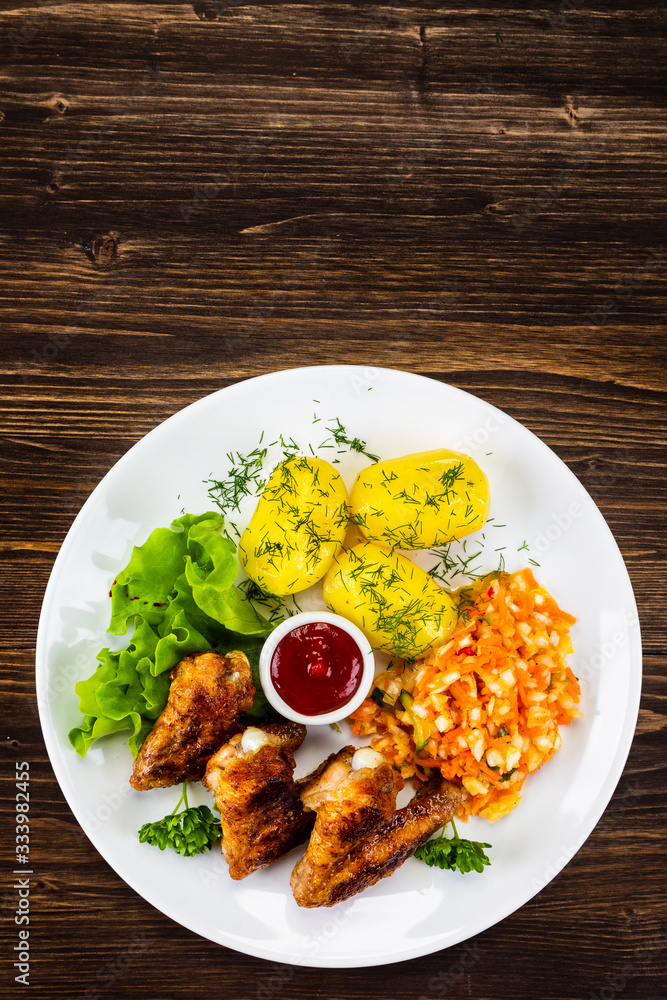 Fried chicken wings with boiled potatoes and vegetable salad on wooden board Fried chicken wings with boiled potatoes and vegetable salad on wooden board